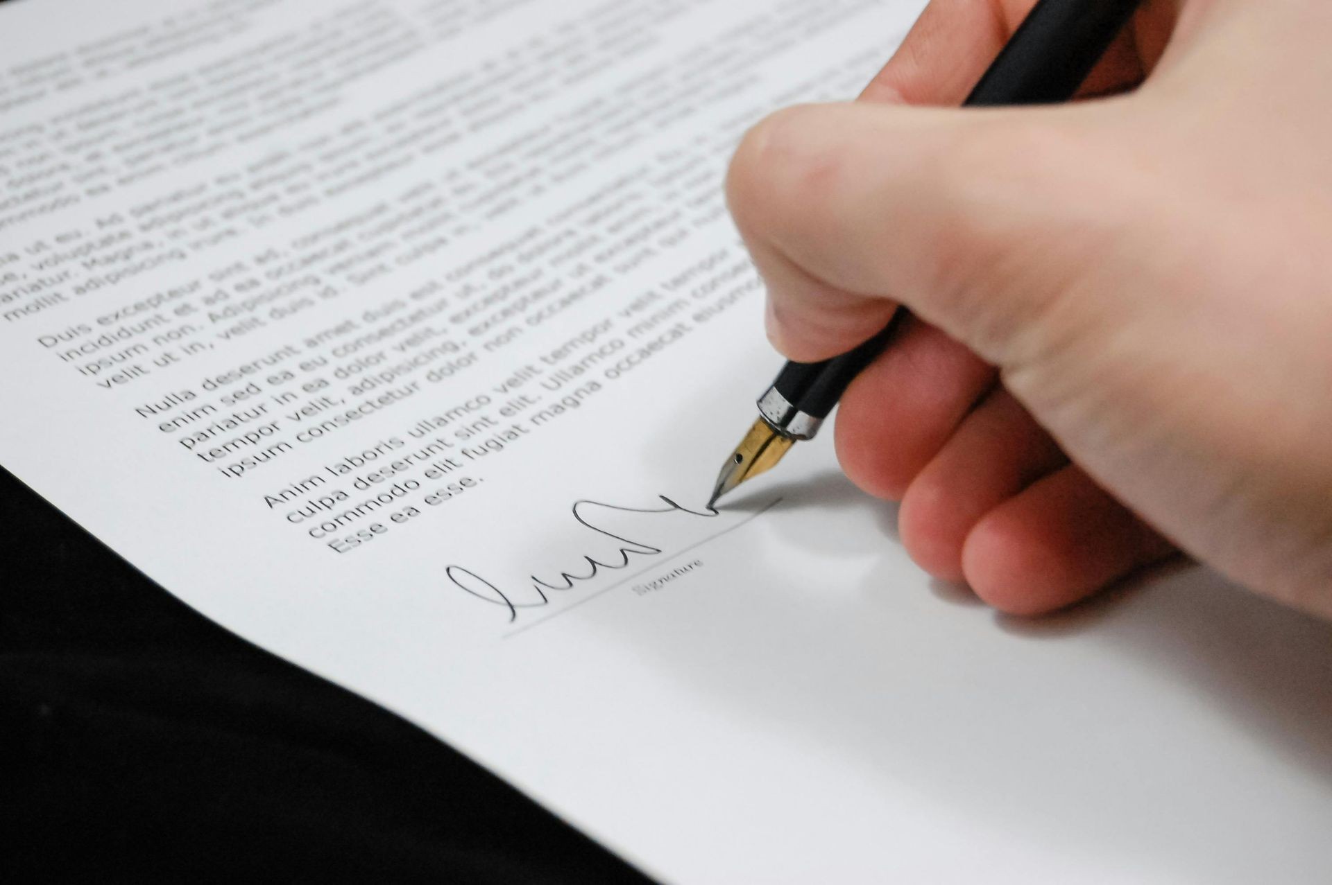 Close-up of a hand using a fountain pen to sign a document filled with text.