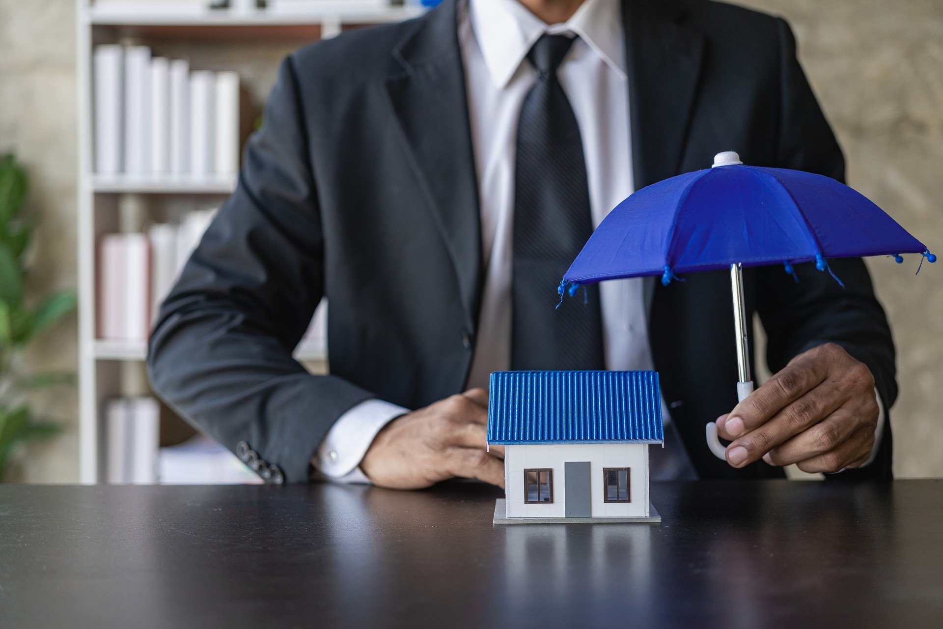 Empresário espalhando guarda-chuva em pequena casa azul, conceito de seguro
