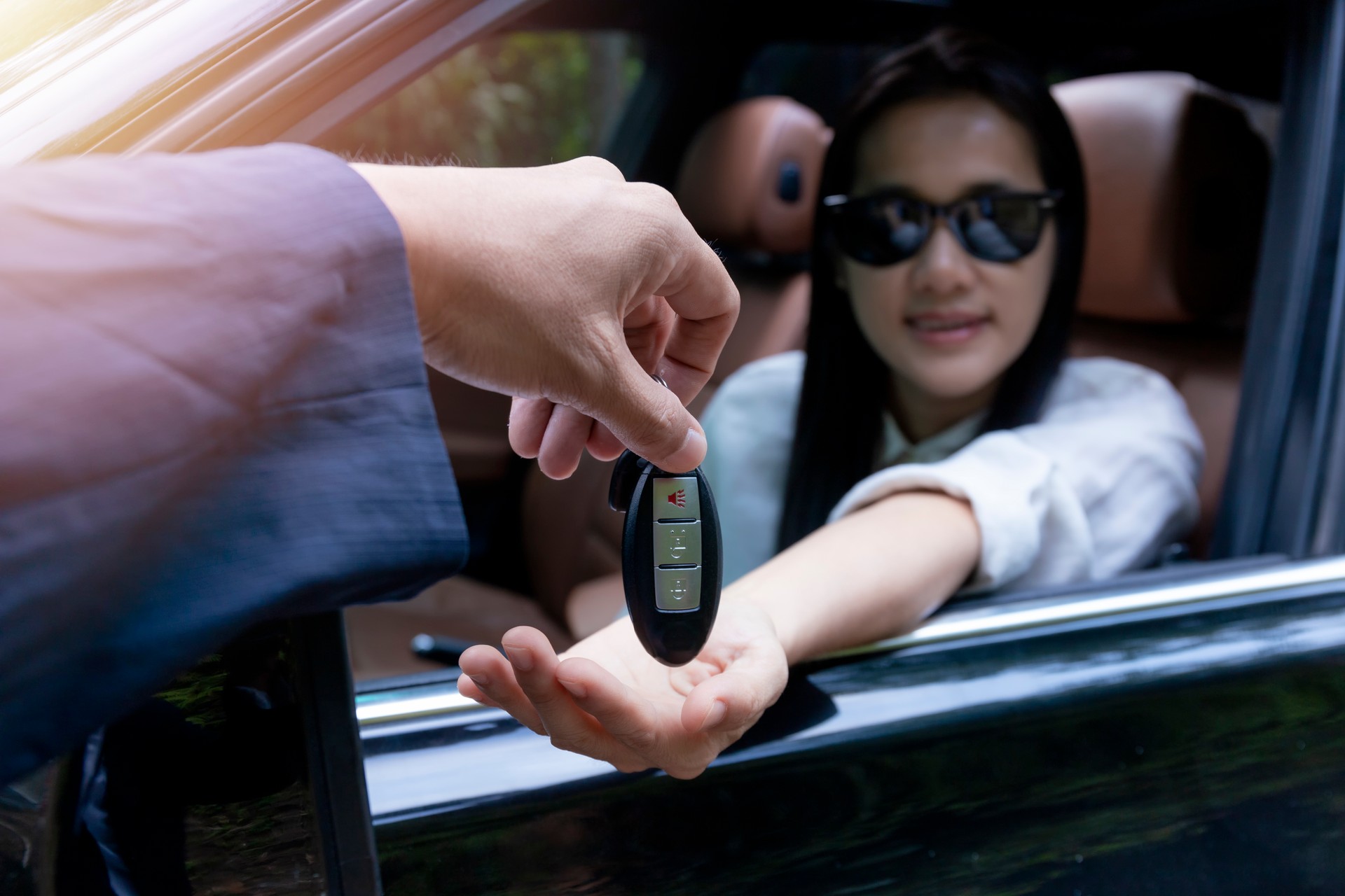 Close up of dealer giving key to new owner car. New car. Auto dealer giving woman automobile key for test drive on country road. Soft focus  smiling women try to test drive a car on road with dealer.